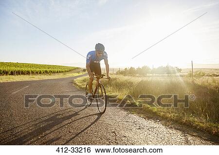 Stock Photograph - Male triathlete cyclist cycling on sunny rural road at sunrise. Fotosearch