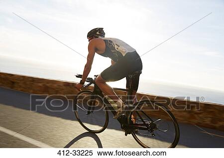 Stock Photography - Male triathlete cyclist cycling on sunny ocean road. Fotosearch