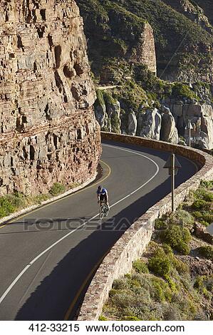 Stock Photography - Male triathlete cyclist cycling uphill along sunny cliffs. Fotosearch