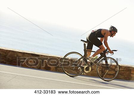 Male triathlete cyclist racing on ocean road View Large Photo Image Stock Image - Male triathlete cyclist racing on ocean road. Fotosearch
