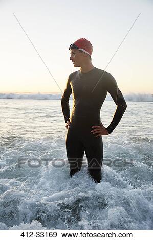 Stock Photo - Male triathlete in wet suit standing in ocean surf. Fotosearch