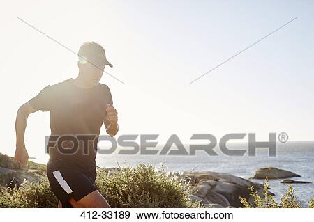 Male triathlete runner running along ocean View Large Photo Image Stock Photo - Male triathlete runner running along ocean. Fotosearch