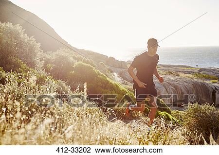 Stock Image - Male triathlete runner running on sunny rocky trail. Fotosearch
