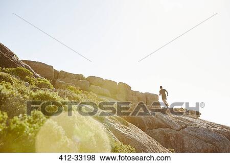 Male triathlete runner running on sunny rocky trail View Large Photo Image Stock Photo - Male triathlete runner running on sunny rocky trail. Fotosearch