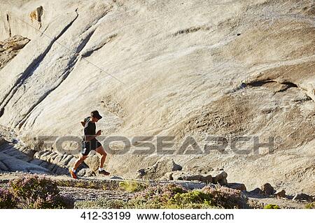 Male triathlete runner running on sunny rocky trail View Large Photo Image Stock Photo - Male triathlete runner running on sunny rocky trail. Fotosearch