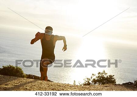 Male triathlete runner running uphill on sunny ocean trail View Large Photo Image Stock Image - Male triathlete runner running uphill on sunny ocean trail. Fotosearch