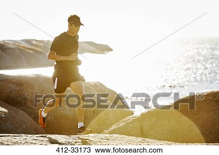 Male triathlete running on rocky trail along sunny ocean View Large Photo Image Stock Image - Male triathlete running on rocky trail along sunny ocean. Fotosearch