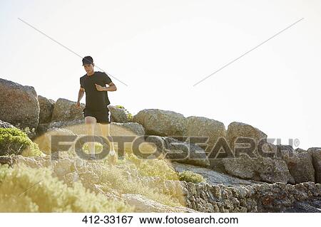 Stock Photo - Male triathlete running on sunny rocky trail. Fotosearch