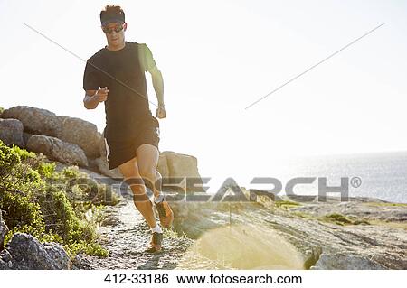 Male triathlete running on sunny rocky trail along ocean View Large Photo Image Stock Photograph - Male triathlete running on sunny rocky trail along ocean. Fotosearch