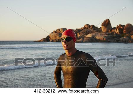 Stock Image - Male triathlete swimmer in wet suit on ocean beach. Fotosearch