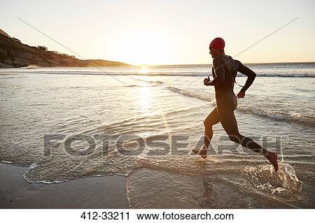 Male triathlete swimmer in wet suit running into ocean surf at sunrise View Large Photo Image Stock Image - Male triathlete swimmer in wet suit running into ocean surf at sunrise. Fotosearch