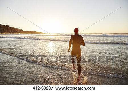 Male triathlete swimmer in wet suit running into ocean surf at sunrise View Large Photo Image Stock Photo - Male triathlete swimmer in wet suit running into ocean surf at sunrise. Fotosearch