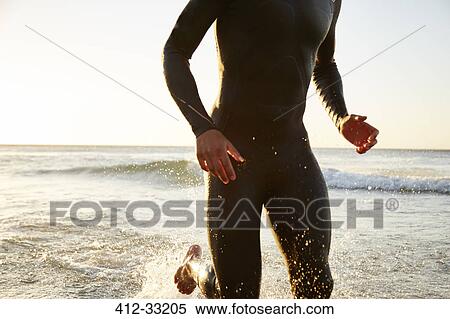 Stock Photography - Male triathlete swimmer in wet suit running out of ocean surf. Fotosearch