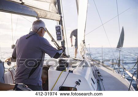 Picture - Man adjusting sailing equipment on sailboat. Fotosearch