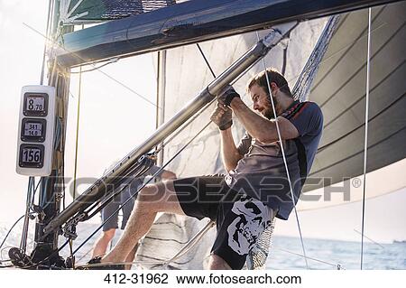 Stock Image - Man adjusting sailing equipment. Fotosearch