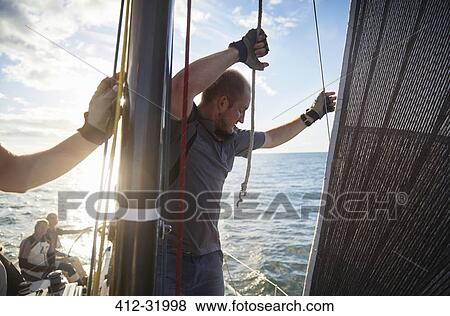 Stock Photo - Man adjusting sailing rigging on sailboat. Fotosearch