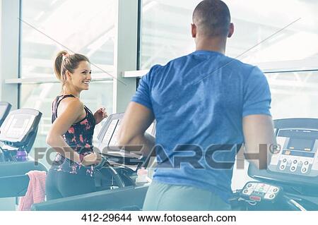 Picture - Man and woman jogging on treadmills at gym. Fotosearch