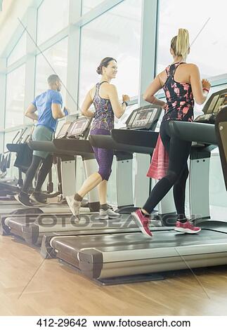 Stock Image - Man and women jogging on treadmills at gym. Fotosearch