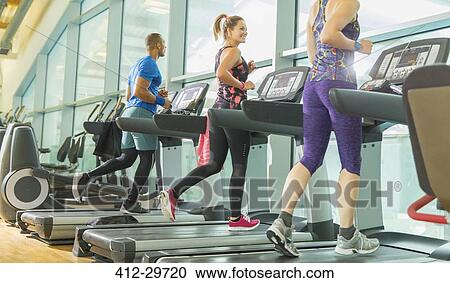 Stock Image - Man and women running on treadmills at gym. Fotosearch