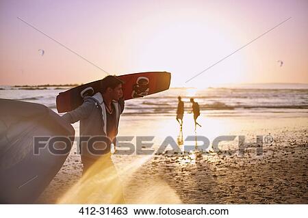 Man carrying kiteboard on sunset beach View Large Photo Image Stock Image - Man carrying kiteboard on sunset beach. Fotosearch