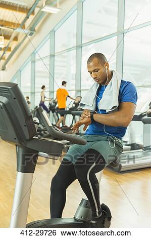 Man checking smart watch on exercise bike at gym View Large Photo Image Stock Photograph - Man checking smart watch on exercise bike at gym. Fotosearch