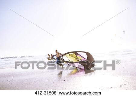 Stock Photo - Man dragging kiteboarding equipment on beach. Fotosearch