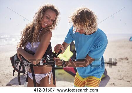 Man fastening kiteboarding safety harness on woman on sunny beach View Large Photo Image Stock Photo - Man fastening kiteboarding safety harness on woman on sunny beach. Fotosearch