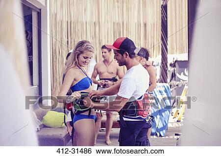 Stock Photograph - Man fastening kiteboarding safety harness on woman. Fotosearch