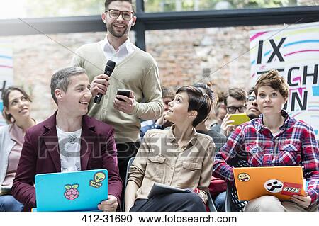 Stock Image - Man in audience asking question with microphone at technology conference. Fotosearch