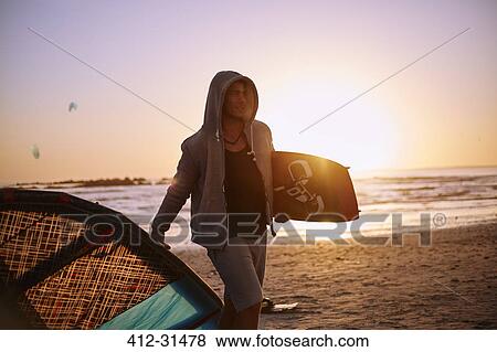 Man in hoody carrying kiteboard equipment on sunset beach View Large Photo Image Stock Photo - Man in hoody carrying kiteboard equipment on sunset beach. Fotosearch
