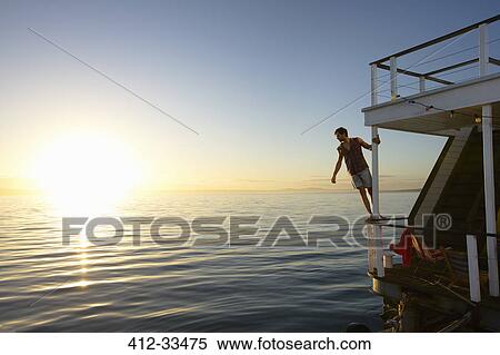 Stock Photography - Man leaning on summer houseboat railing over sunset ocean. Fotosearch
