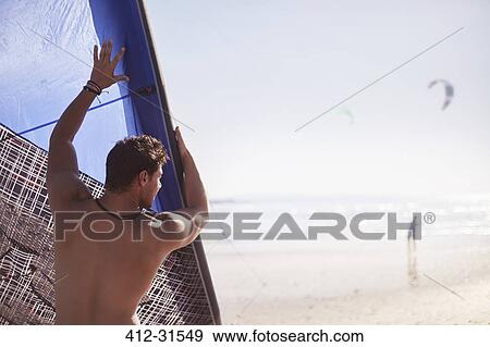 Stock Photo - Man lifting kiteboarding kite on sunny beach. Fotosearch