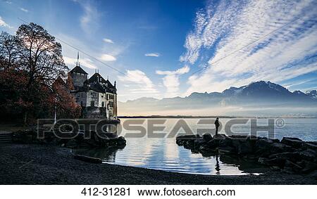 Stock Image - Man on rocks at lakeside outside Chillon Castle, Switzerland. Fotosearch