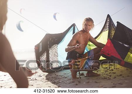 Stock Image - Man preparing kiteboarding kite on sunny beach. Fotosearch