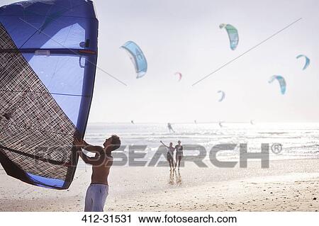 Stock Image - Man preparing kiteboarding kite on sunny beach. Fotosearch