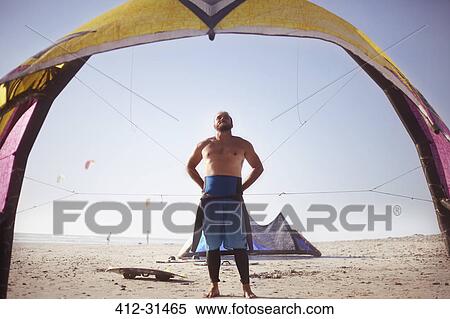 Stock Photography - Man preparing to kiteboard on sunny beach. Fotosearch
