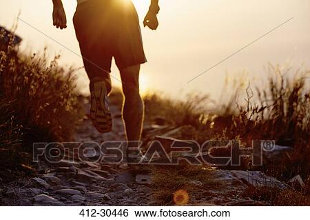 Stock Photograph - Man running on craggy trail at sunset. Fotosearch