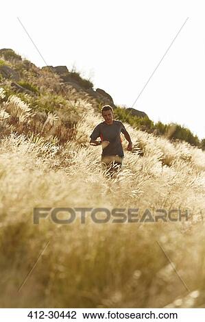 Stock Image - Man running through tall sunny grass. Fotosearch