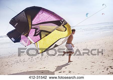 Stock Image - Man running with kiteboarding kite on sunny beach. Fotosearch