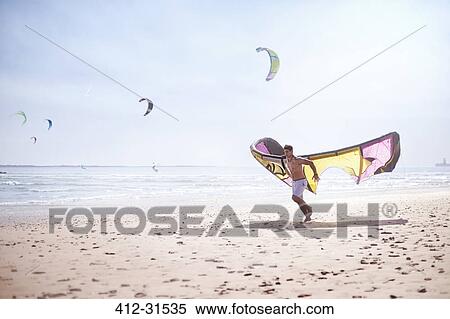 Stock Photography - Man running with kiteboarding kite on sunny beach. Fotosearch