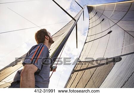 Stock Image - Man sailing looking up at sail. Fotosearch