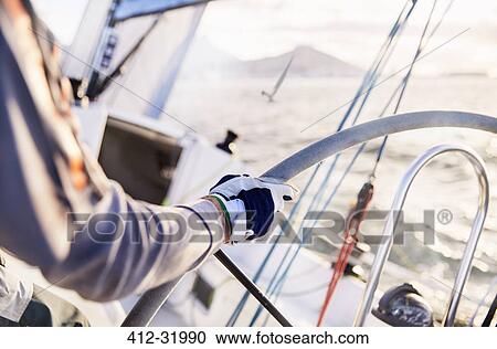 Stock Image - Man sailing steering sailboat at helm. Fotosearch