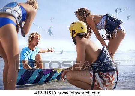 Stock Image - Man teaching friends kiteboarding on sunny beach. Fotosearch