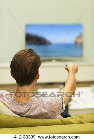 Man watching TV changing channels on living room sofa View Large Photo Image Stock Photo - Man watching TV changing channels on living room sofa. Fotosearch