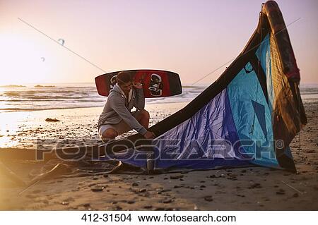 Picture - Man with kiteboarding equipment on sunset beach. Fotosearch