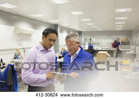 Picture - Manager and engineer looking at clipboard in steel factory office. Fotosearch