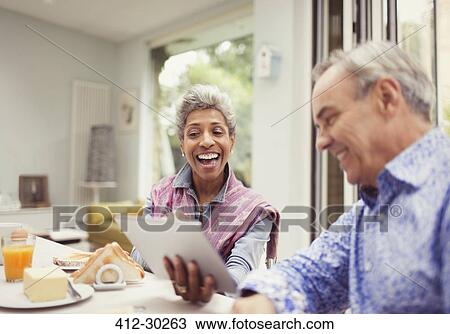 Mature couple laughing and using digital tablet at breakfast table View Large Photo Image Stock Image - Mature couple laughing and using digital tablet at breakfast table. Fotosearch