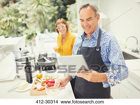 Mature couple with digital tablet cooking in kitchen View Large Photo Image Picture - Mature couple with digital tablet cooking in kitchen. Fotosearch