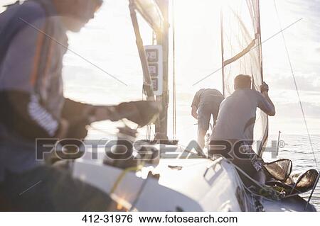 Stock Photograph - Men adjusting sailing equipment on sailboat. Fotosearch