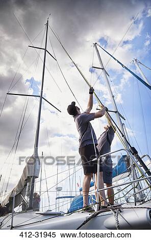 Stock Photography - Men adjusting sailing equipment on sailboat. Fotosearch